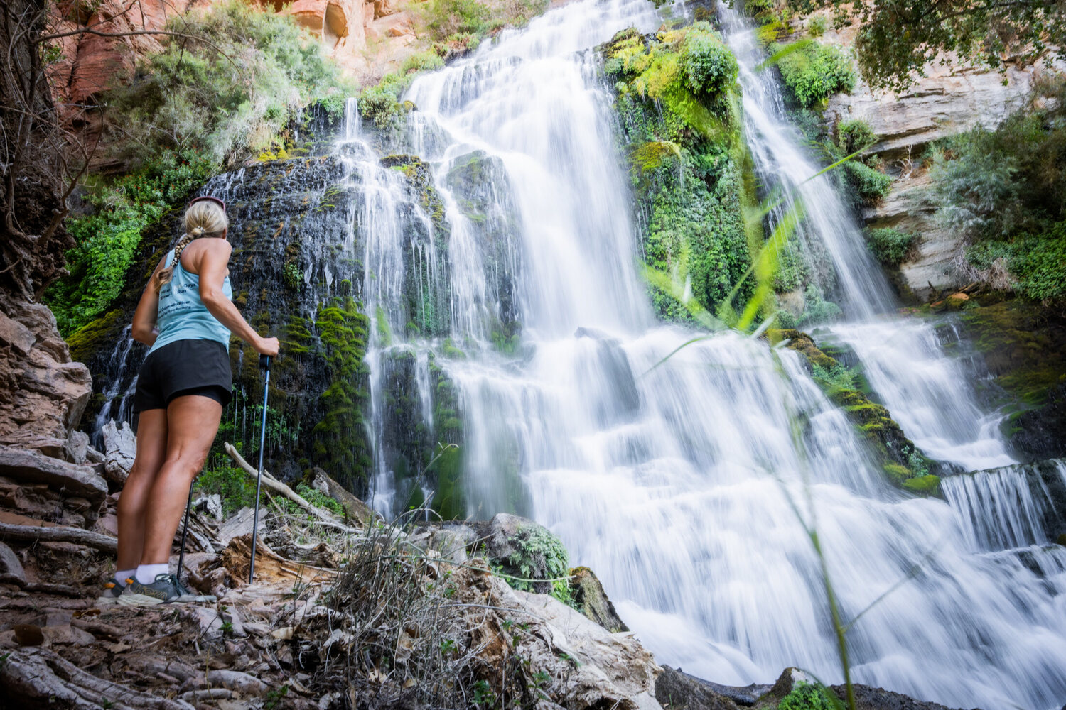 A hiker standing at the base of a tall waterfall dropping through the red rock of the Grand Canyon