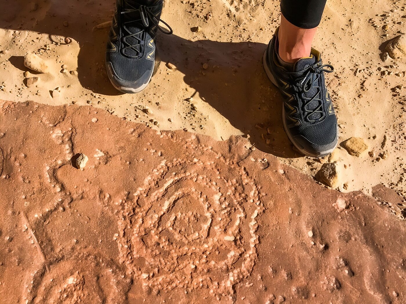 Thousand-year-old petroglyphs pecked into the sloping sandstone floor of the Mansard alcove, a hiker's boots beside them for scale