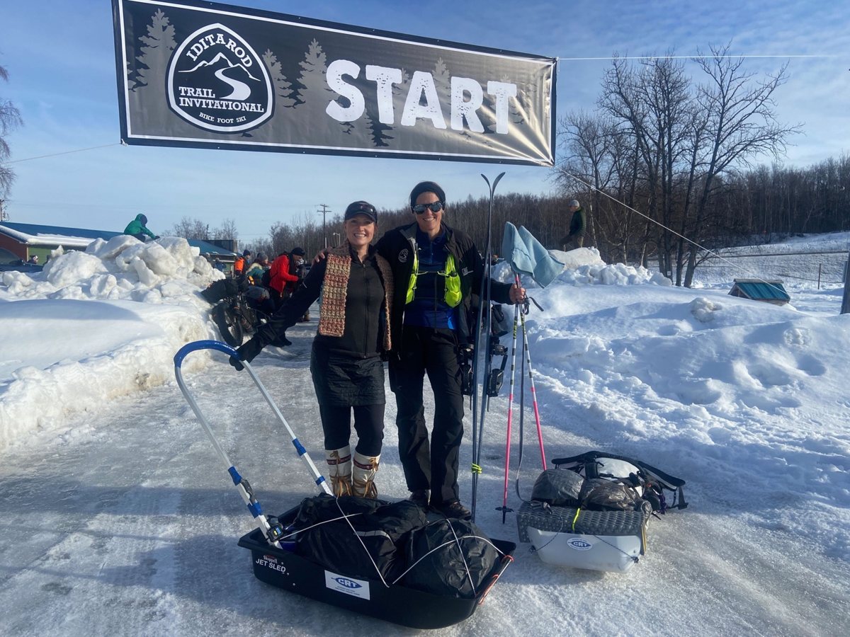 Two racers with sleds under the START banner of the Iditarod Trail Invitational