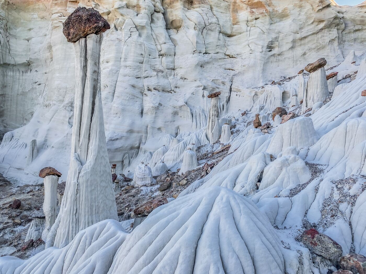 A tall single tower in the foreground with more hoodoos and the flowing white base behind it