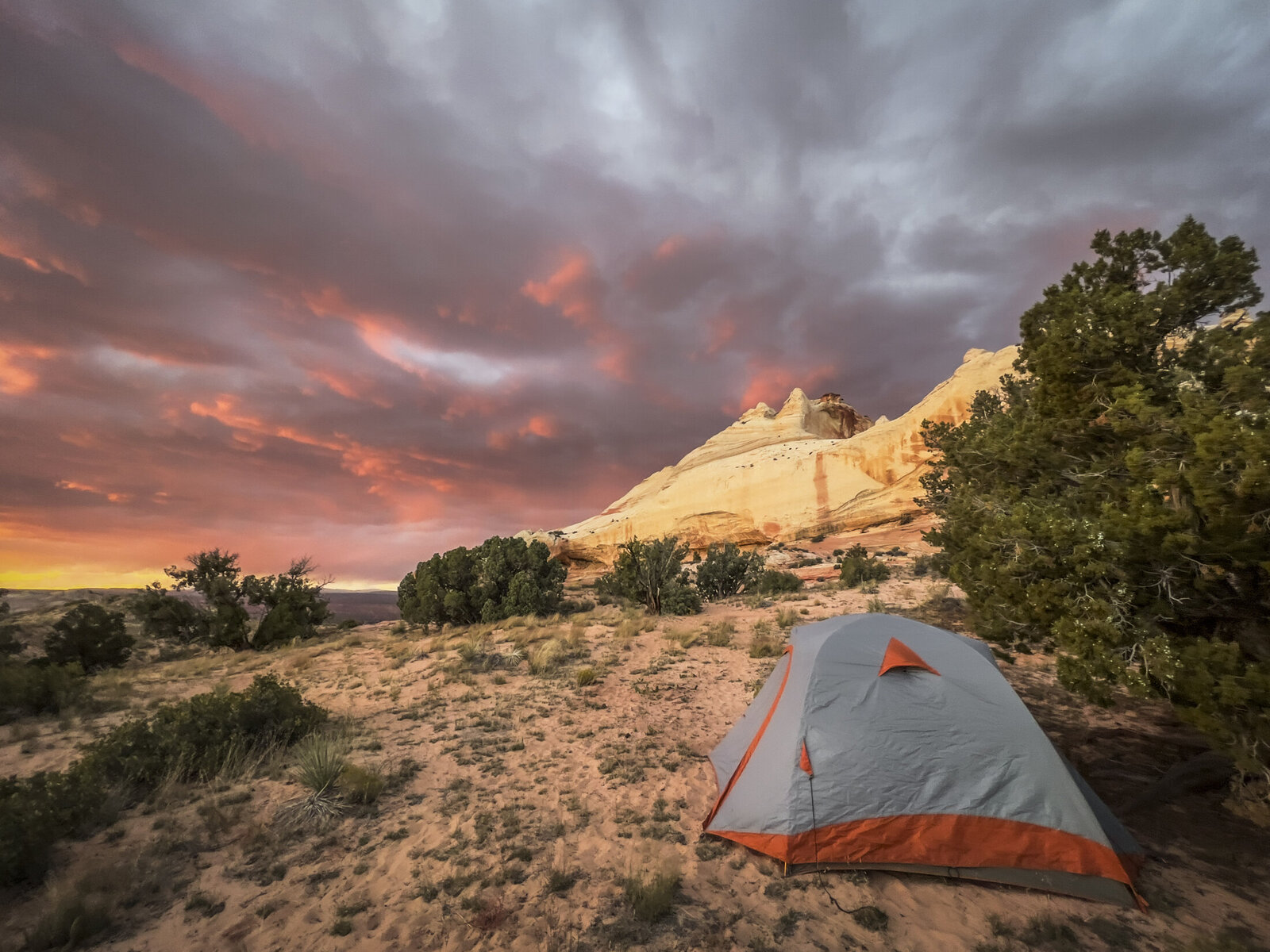 A dramatic pink-and-orange sunset over a tent and the pale sandstone at White Pocket